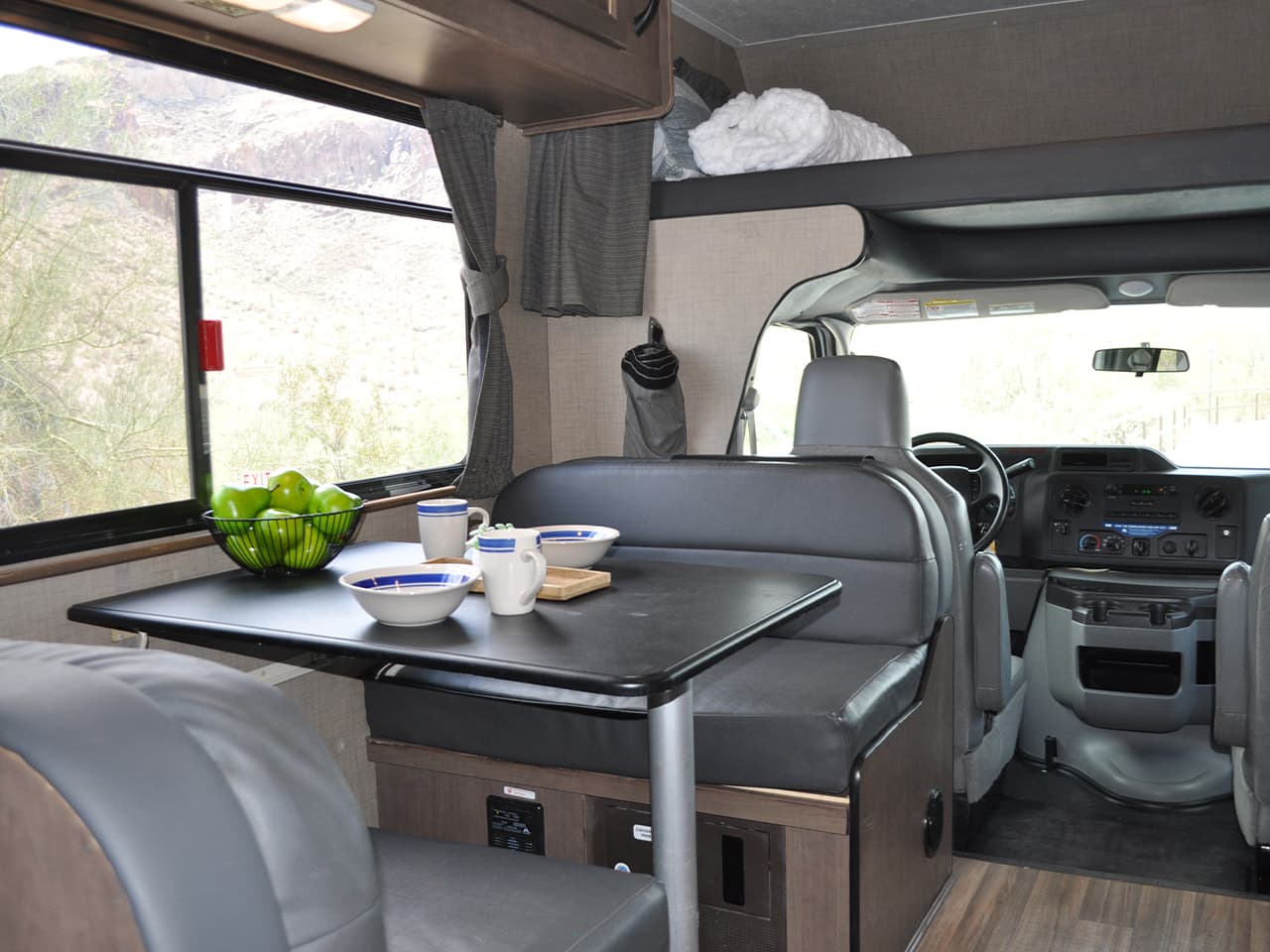 Forward view of drivers area, storage area above driver and passengers seats converted to bed, and assembled dining area behind drivers seat